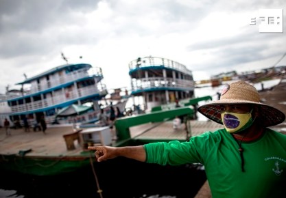 Un hombre con tapabocas de diseño de la bandera brasileña señala hacia el río Amazonas en Manaos (Brasil). EFE/ Raphael Alves