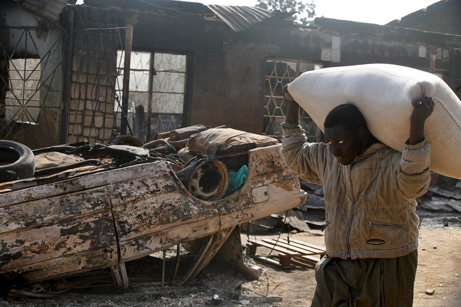 Un hombre pasa cargado con un saco junto a los restos de un coche incendiado, en la ciudad nigeriana de Jos, epicentro de enfrentamientos entre musulmanes y cristianos, el 22 de enero de 2010.